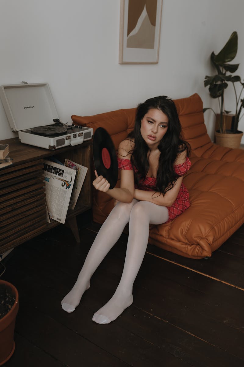 A fashionable adult woman sitting with a vinyl record in a vintage themed living room.